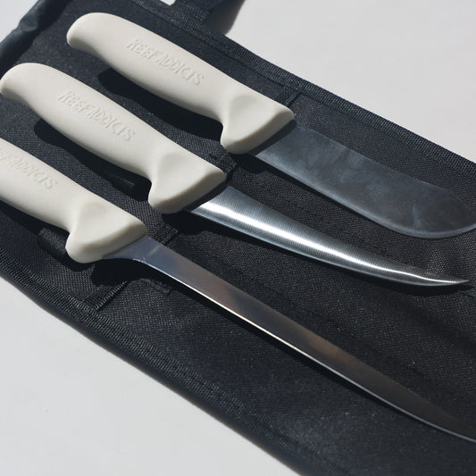 A set of three fishing knives with white handles laid out on a black surface.